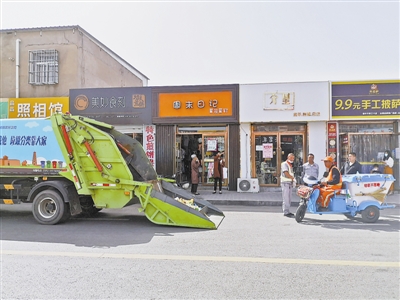 图为垃圾清运车在商户门前等待清运垃圾。